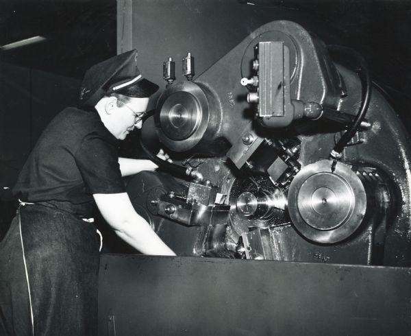 A female factory worker wearing an apron readies a shell turning machine for operation at International Harvester's New Brighton Works.