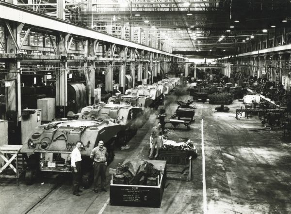 Men stand in a factory, possibly the Bettendorf Tank Arsenal, used during World War II to repair tanks for the United States military.