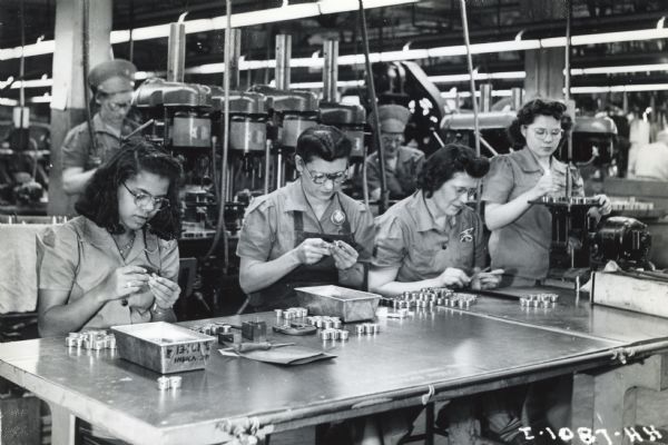 Female factory workers on a production line at International Harvester's West Pullman Works. The women inspect small metal parts used in war production.