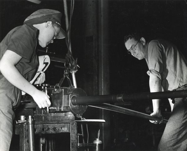 Factory worker James Matzke raises the barrel of a 20mm cannon onto a receiving block to be inspected by Beverly Ackerman at International Harvester's St. Paul Works.