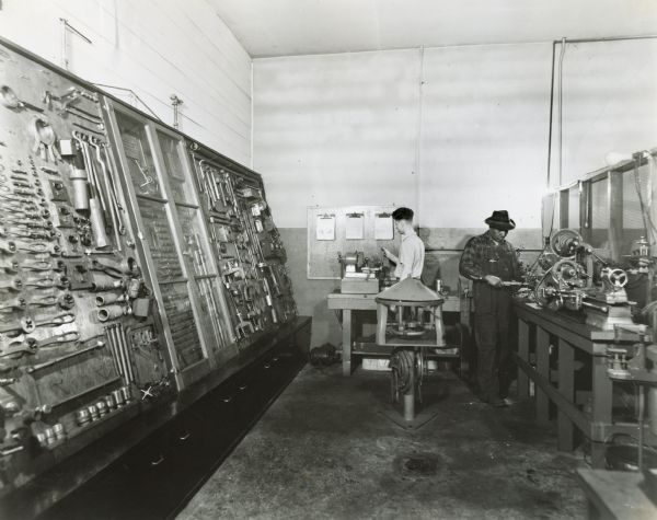 William Gardner working at a grinder, and Otto Varbrough(?) working at a pin fitting machine in the tool room of an International Harvester dealership. A large rack of hand tools runs along one of the walls.
