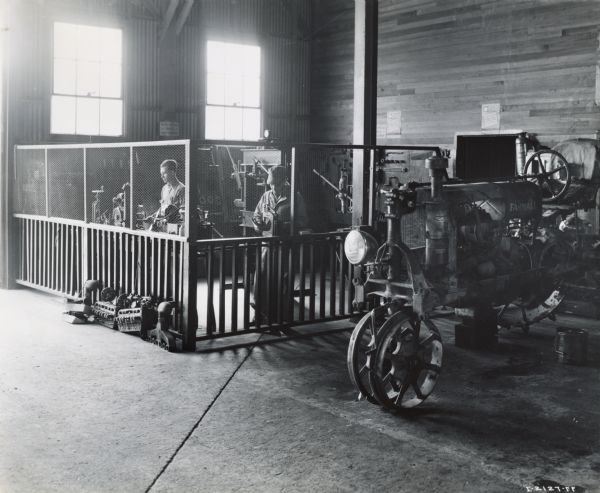 Mechanics work near a Farmall Tractor in the service shop of an International Harvester dealership. A sign on the back wall near the windows reads: "We Do NOT Loan TOOLS or SHOP EQUIPMENT."