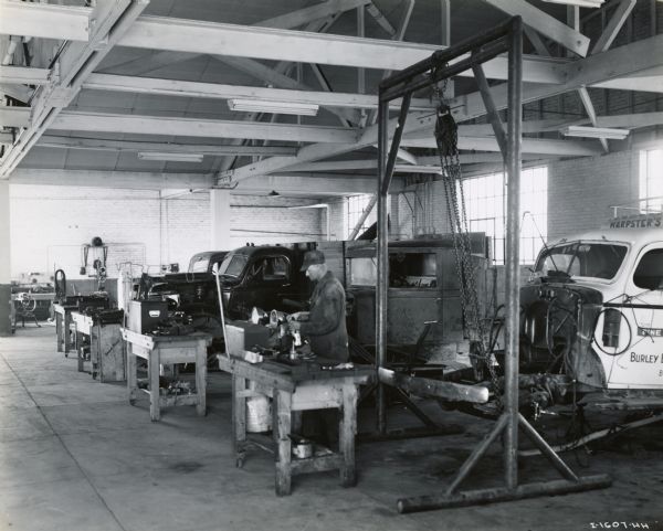 A mechanic works on a truck at Chisholm Brothers, an International Harvester dealership in Snake River Valley, Idaho. On the right the front of a truck chassis is suspended from a pulley.