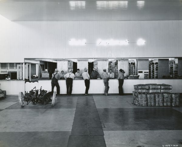 Men standing at a parts counter at the Buhl Implement Company, an International Harvester dealership in the irrigated Snake River Valley. On the far left a woman is working in a separate office.