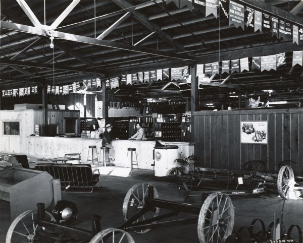 Showroom floor and service counter of the Brown Tractor Company, an International Harvester dealership. Two men are at the service counter. Advertising posters and banners are posted throughout the showroom. The dealership was operated by Burr Brown and A.E. Greiner.

