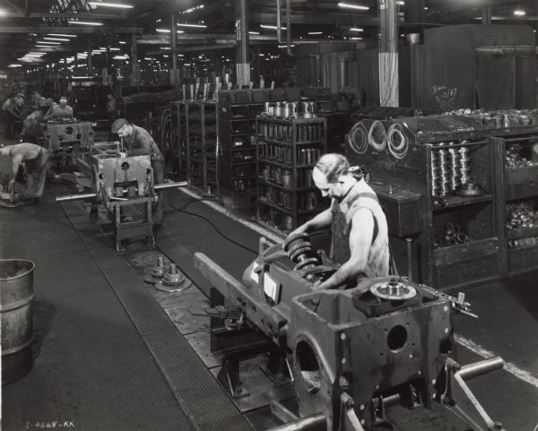 Factory workers on a crawler tractor (TracTracTor) assembly line at International Harvester's Tractor Works. Behind the men are shelves filled with small machine parts.