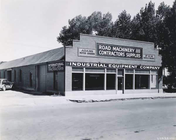 View from road of the storefront of the Industrial Equipment Company, an International Harvester dealership. Signs on the building read: "International TracTracTors," "Adams Motor Graders," "Road Machinery and Contractors Supplies," and "P&H Shovels and Welders."