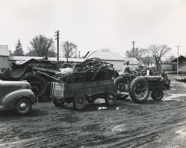 John De Roy pulling a trailer load of scrap metal with a Farmall-H tractor. The metal was collected as part of a scrap drive.