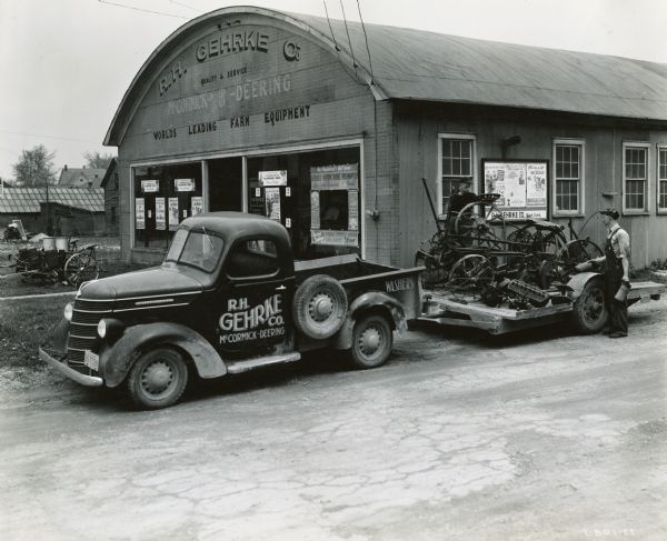 International truck with a trailer full of scrap metal parked outside the R.H. Gehrke Company, an International Harvester dealership. William Le Capitaine, Jr. and Robert McGlen, mechanic and helper, are loading the metal as part of a scrap drive.