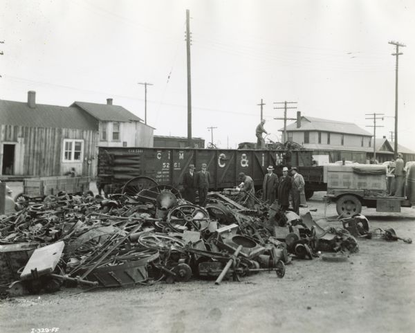 Men watch as workers cut down scrap iron and load it on a railroad car as part of a wartime scrap drive.