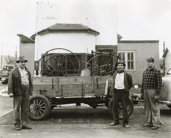 Three men stand near a trailer while weighing in a load of scrap iron brought from a farm by William Gory (at far right). At left is Jim Barrett, manager of the Rickle Grain Company, which advanced cash to farmers for their scrap. Standing in the center with a pipe in his mouth, is Walt Sullivan, a county war board member. The Barton County, Kansas farm scrap drive netted 550 tons in the first week.