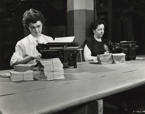 Two women using typewriters at a large table.
