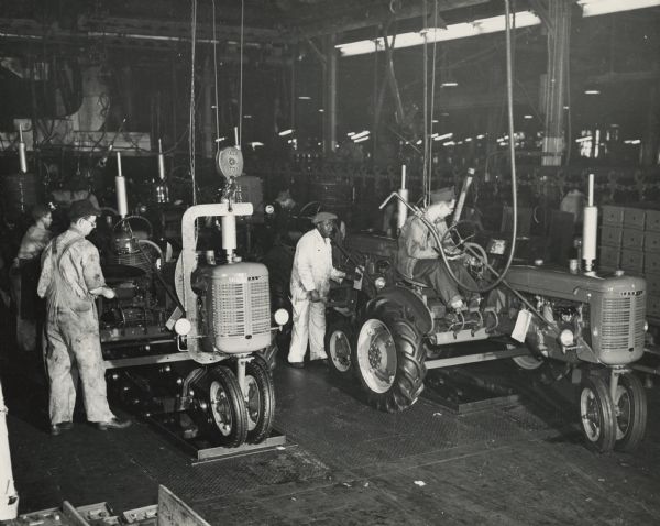 Factory workers with tractors on the end of the Farmall assembly line at International Harvester's Tractor Works.