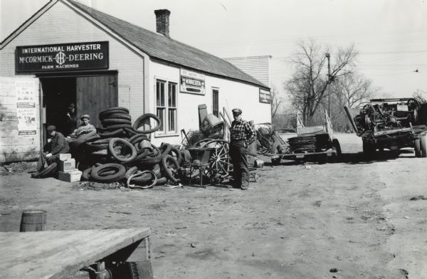 International Harvester dealer Allan Halvorson (center) standing next to a pile of scrap metal and rubber near his dealership building. The materials were collected for a wartime scrap drive.