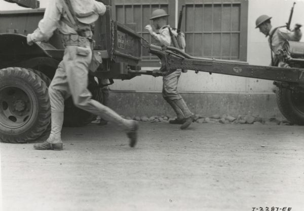 Marines running to climb aboard a truck after coupling a 75-mm gun.