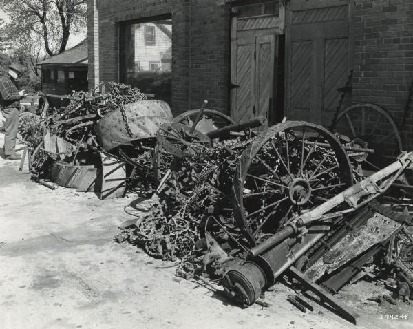 A man stands near scrap metal piled beside a dealership building. The metal was collected for a war time scrap drive.