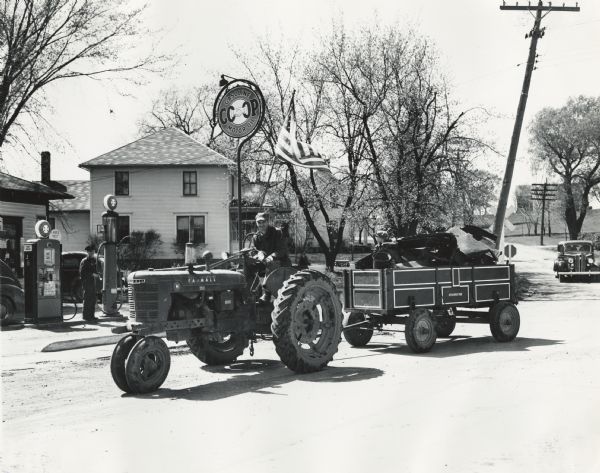 Helmuth Strobush and his son Jerry haul scrap metal with a Farmall H tractor and a McCormick-Deering farm wagon. The tractor is parked near a co-op service station. Strobush and his son were participating in a wartime scrap drive.