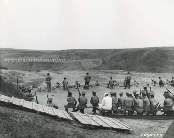 U.S. Marines training at a rifle range, possibly at a Marine Corps firing range. A row of targets is on a hill in the background.