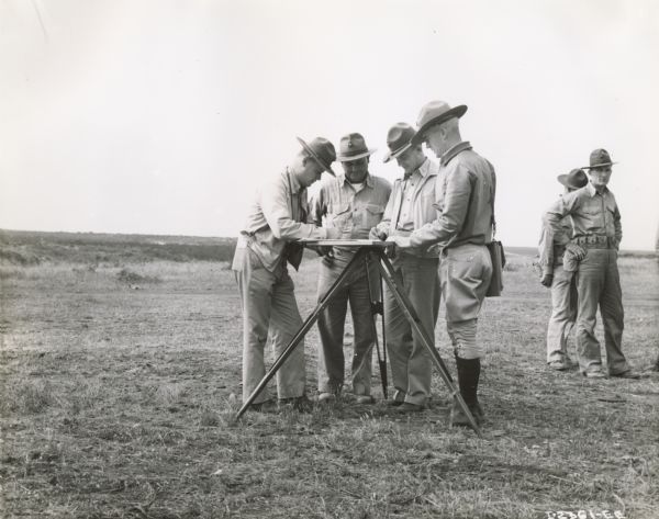 Marines using a plane table to figure firing data at an artillery range at Camp Elliot, near San Diego. The men of the 10th Marines standing around the table are First Lieutenant John S. Twitchell, Battery H (left); Platoon Sargeant G.B. Respress, Battery I (facing camera, looking down at table); Second Lieutenant George B. Thomas, Headquarters and Service Battery; and First Lieutenant William T. Wingo, Jr., Battery G.