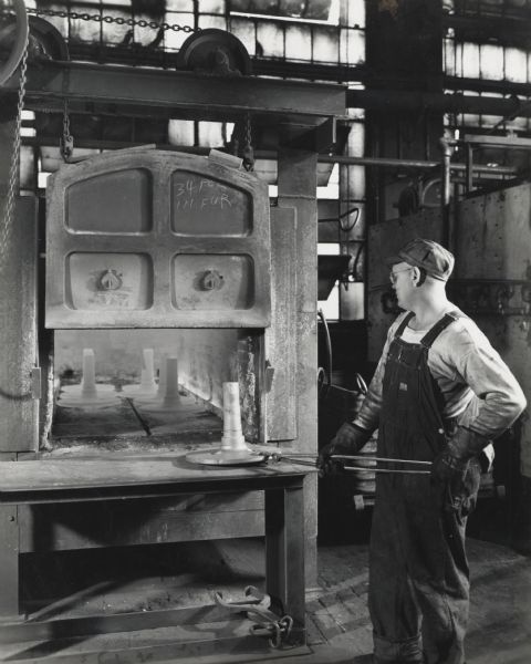 Factory worker hardens tractor parts in "one of a battery of gas-fired box type heat treating furnaces."