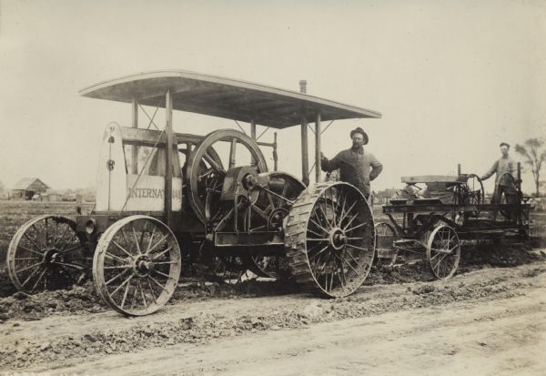 Two men with an International friction drive tractor and a road grader. According to the original caption, the tractor was "made in 1907" and was "still in use" by Joseph Bammel at the time the photograph was taken.