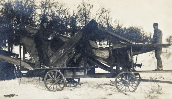 Henry Dinkler and his brother with a Buffalo Pitts separator (thresher). They are outdoors in the snow near a row of trees.