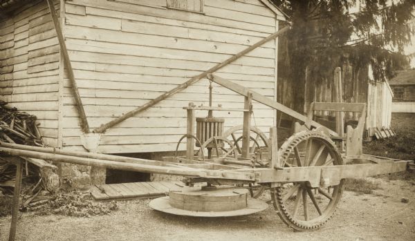 A mowing machine designed by Jabez Baily in yard outside a house or farm building.
