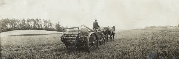 Panoramic view from the rear of man on manure spreader drawn by two horses in field.