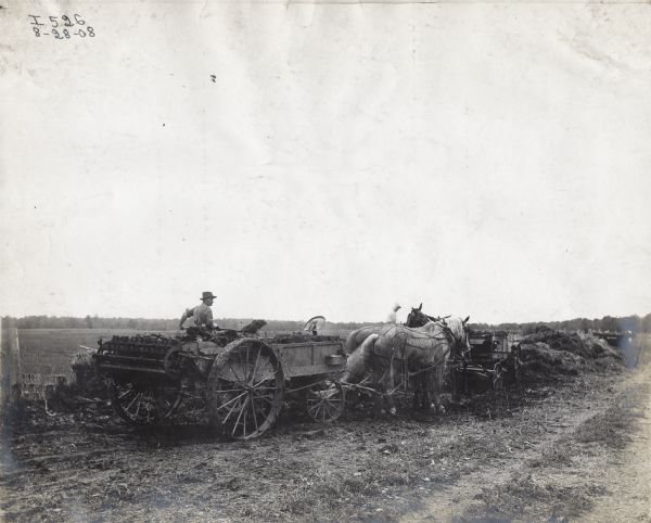 Men loading horse-drawn manure spreaders on farm land.