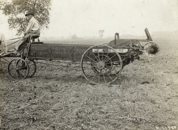 Farmer in a field seated on a horse-drawn No. 8 Low Corn King manure spreader.