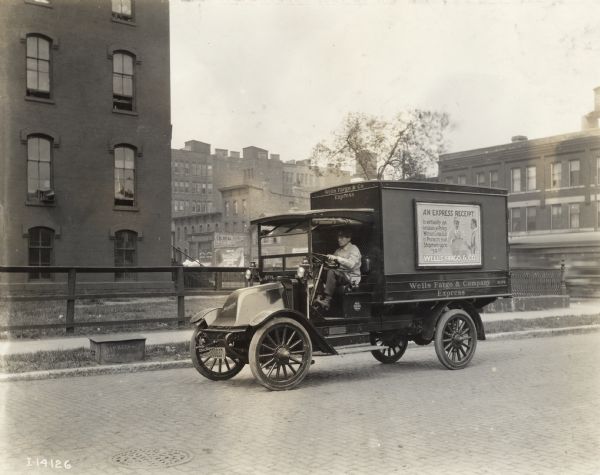 Man drives an International Model F or 31 truck used by Wells Fargo & Company Express for deliveries. The side of the truck has an advertisement for the Express Receipt which protects shipments up to $50.00.