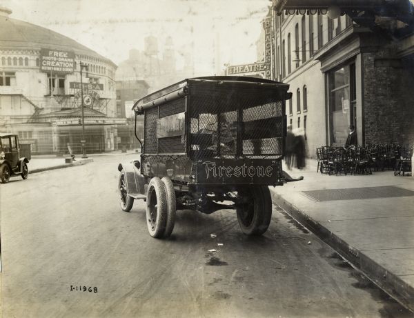 Rear view of International Model F or 31 truck operated by Firestone. The truck is parked on a city street in front of  buildings. The Firestone company logo is printed on the rear of the truck bed. Nearby is the Blackstone Theatre, now known as the Merle Reskin Theatre. Across the street is a large International Bible Students Association building.