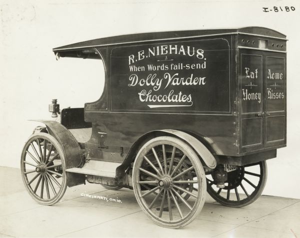 International Model M truck operated by R.E. Neihaus confections. The side of the truck advertises Dolly Varden chocolates. The rear door bears text: "Eat Acme Honey Kisses."