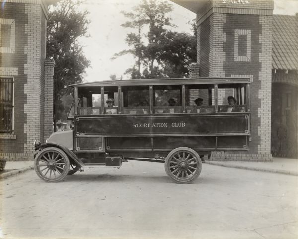 International Model F or 31 truck used as a bus for a recreation club. A small group of men are sitting inside the bus, and a building with an arched entrance is in the background.