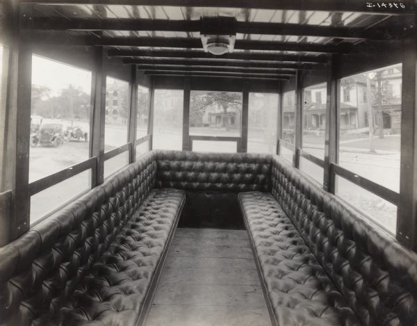 Interior of an International Model F or 31 truck equipped as a bus. Seating consists of one center aisle with two rows of cushioned seats along the sides of the vehicle which is lined with large windows.