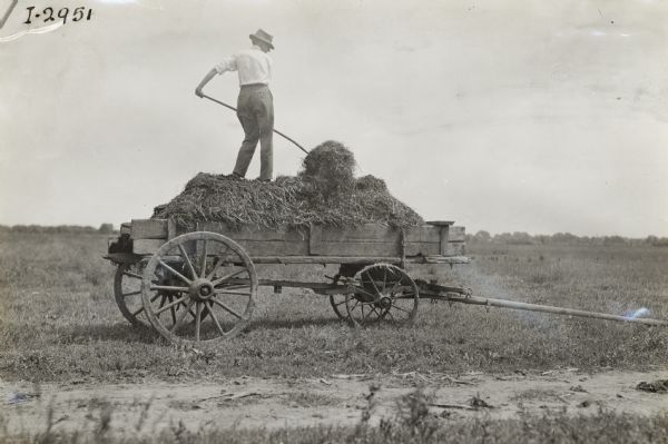 Man shoveling manure while standing on a manure spreader or farm wagon.