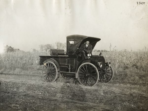 A man is leaning out of an International Model M truck near a cornfield.