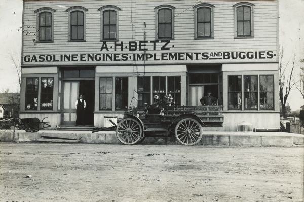 View across the road of three men and an International Model M truck outside the A.H. Bentz farm equipment dealership. A sign on the building advertises gasoline engines, implements, and buggies.