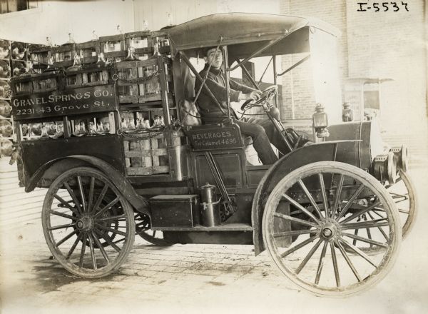 Man driving an International Model M truck for Gravel Springs Co. water supply. The truck is loaded with crates of water jugs.