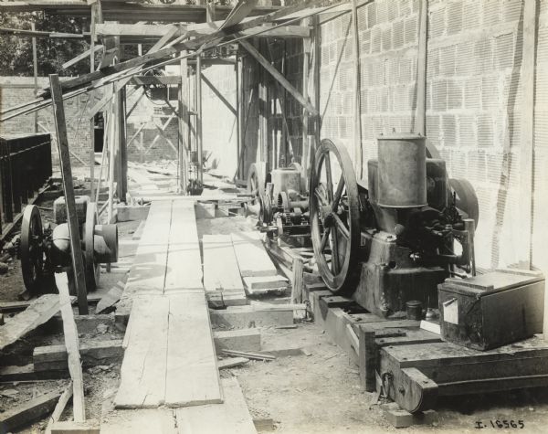 Stationary engines of various sizes mounted on skids or planks of wood. The engines appear to be situated among scaffolding and an unfinished wall at what may be a construction site.