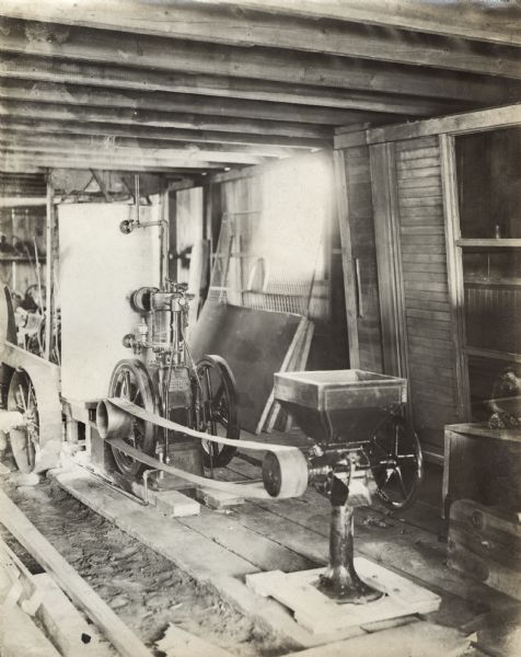 Stationary engine belted to a feed grinder in a wooden shed.