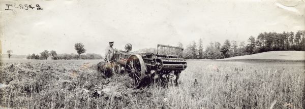 Panoramic view of two men loading a horse-drawn manure spreader (possibly a Kemp) in a field.