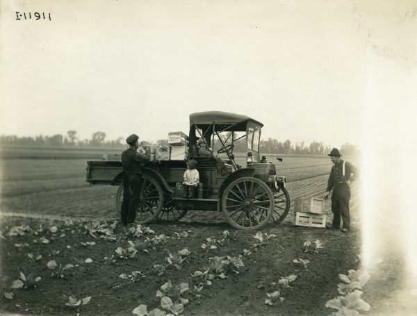 International Model M truck used by Terpstra & Son for garden crop shipments. Two men load the truck bed with crates for shipment of what appears to be a radish crop. Two small girls sit on the truck.