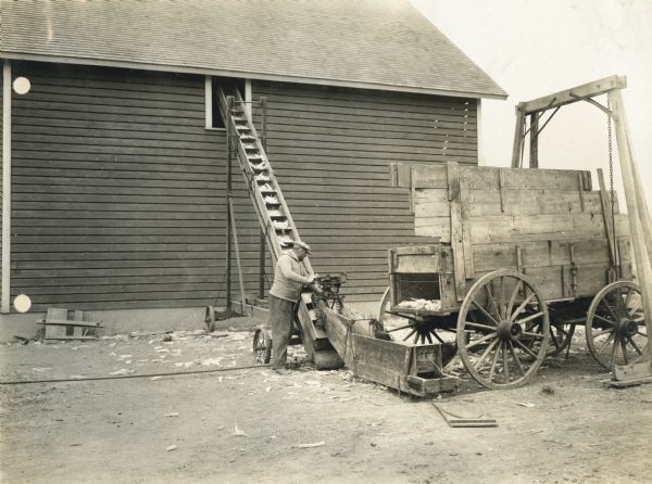 Farmer using a Titan engine to power an elevator into a corn crib from a wagon.