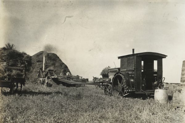Men in a field threshing with a stationary thresher powered by a Titan 18-35.