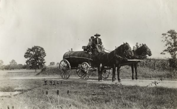 Man with two boys, possibly father and sons, seated on a water wagon pulled by a team of horses along a rural dirt road.