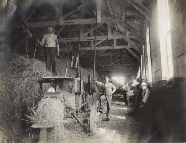 Several men inside a barn baling hay with a power hay press.