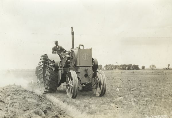 Man plowing with International 15-30 or 12-24(?) tractor on farmland. Another man is standing behind the tractor.