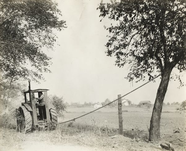 A farmer has chained his International 15-30 or 12-24(?) tractor to a tree to pull it down.