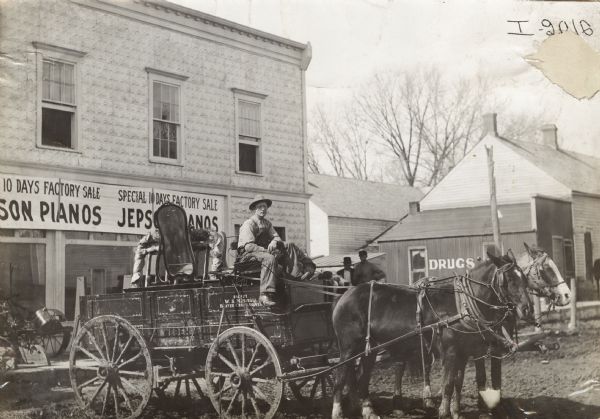 Man seated outside the Jepson piano store in a horse-drawn Weber wagon loaded with items, including a mirror.